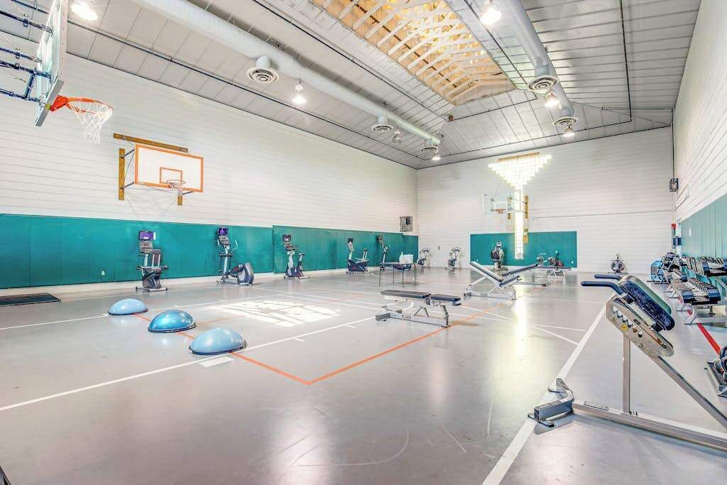 Un gimnasio con un aro de baloncesto, equipamiento de ejercicio y un amplio espacio abierto.