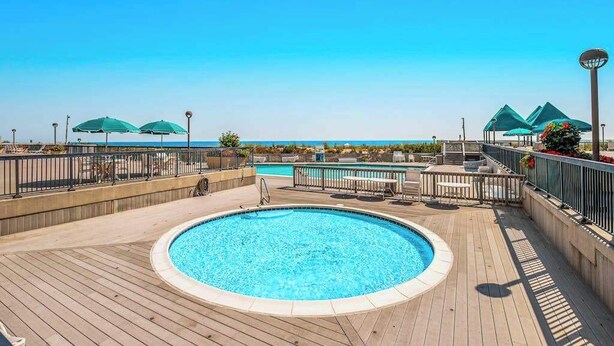 Un espace piscine avec vue sur l’océan, des chaises longues et des parasols.