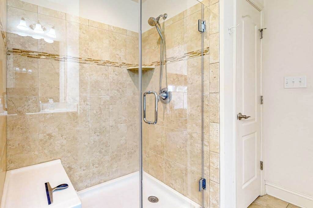 A glass-enclosed shower with a handheld showerhead, a white door, and a tiled wall.