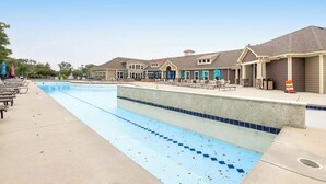 Una piscina con lettini e ombrelloni, circondata da edifici dallo stile architettonico uniforme.