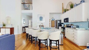 Une cuisine moderne avec des meubles blancs, un îlot central doté de tabourets de bar et un coin repas avec un canapé bleu.