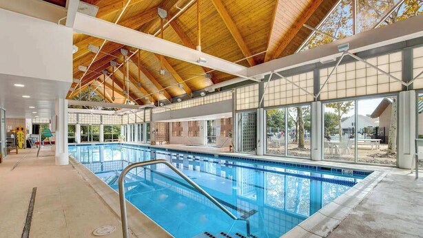 Une piscine intérieure dotée d’un plafond en bois, de grandes fenêtres et offrant une vue dégagée sur l’extérieur.