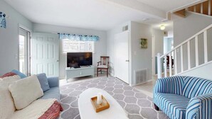 Una sala de estar con un sofá, un televisor, una silla y una escalera.
