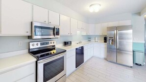 Una cocina moderna con armarios blancos, electrodomésticos de acero inoxidable y piso de tono claro.