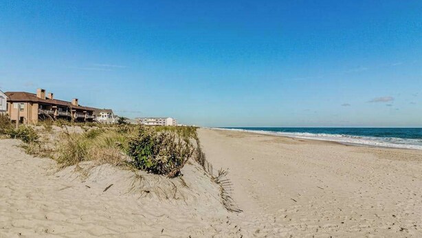 Una playa con un edificio a la izquierda, arena y océano.