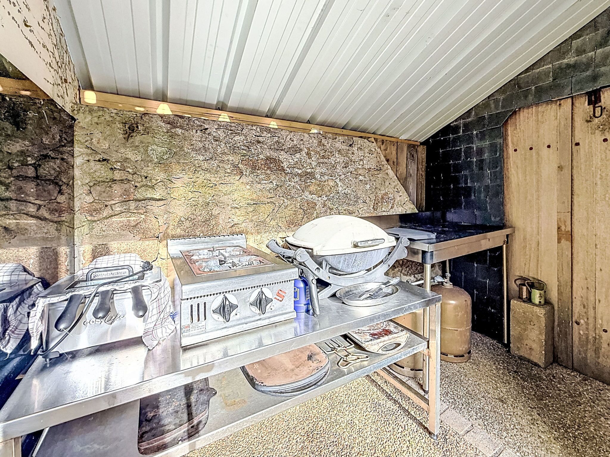 Una cocina con estufa a gas, hervidor y fogón portátil sobre una encimera de metal.