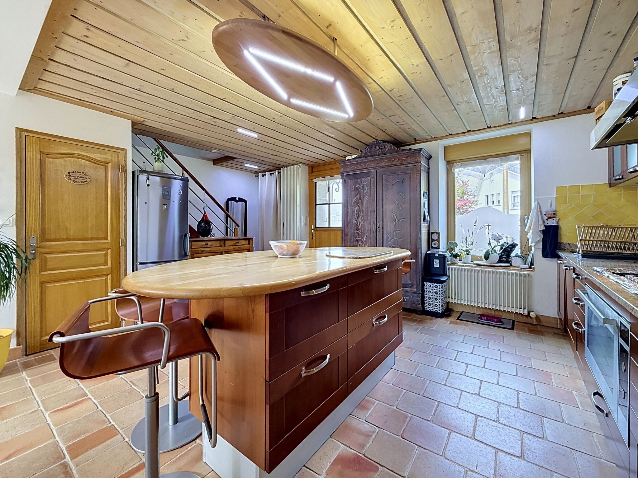 A kitchen with a wooden ceiling, a central island, a refrigerator, and a window.