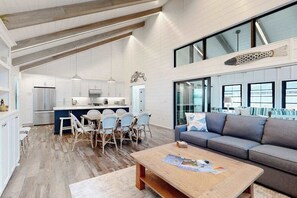 A spacious living area with a sofa, a coffee table, and a dining area with chairs. - Town of Dewey Beach modern home with grill & outdoor showers - prime location (Dewey Beach)