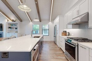 A modern kitchen with white cabinetry, a central island, stainless steel appliances, and pendant lighting. - Town of Dewey Beach modern home with grill & outdoor showers - prime location (Dewey Beach)