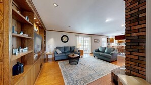A living room with two sofas, a coffee table, wooden shelves, a clock, and a window. - Town of Dewey Beach house near golf with fireplace & fenced yard - dog-friendly (Dewey Beach)