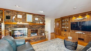Un salon avec une cheminée en briques, un canapé en cuir, un meuble de rangement en bois et un téléviseur à écran plat.