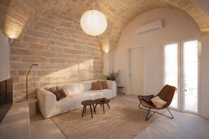 Ein Wohnzimmer mit Steinwand, einem weißen Sofa, einem braunen Sessel, einem Couchtisch und einer Pendelleuchte.