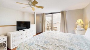 Ein Hotelzimmer mit Bett, Fernseher, Deckenventilator, einem Fenster mit Vorhängen und Blick nach draußen.