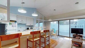 A modern kitchen with white cabinets, a wooden bar area with stools, a large window, and a television. - Sea Colony Tennis 1st floor condo w/ pool, free WiFi, and gym (Bethany Beach)