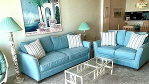 Ein Wohnzimmer mit zwei blauen Sofas, einem Glastisch und einem Bild an der Wand.