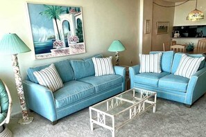 Ein Wohnzimmer mit zwei blauen Sofas, einem Glastisch und einem Bild an der Wand.
