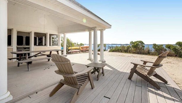 A covered outdoor area with wooden chairs and tables, a picnic table, and a view of the beach and ocean. - Salt Meadows townhouse w/ elevator, gas fireplace & community pool and pier (Fenwick Island)