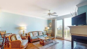 A living room with a fireplace, wicker furniture, and a television. - Salt Meadows townhouse w/ elevator, gas fireplace & community pool and pier (Fenwick Island)
