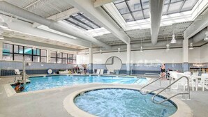 Una piscina interior con jacuzzi, sillas de descanso y pared de azulejos.