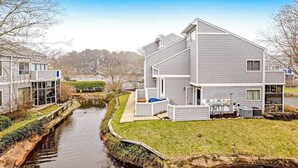 Una casa moderna de dos pisos con un pequeño jardín delantero, una unidad exterior visible y un estrecho canal de agua.