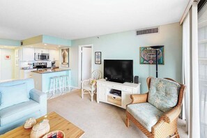 A living room with a sofa, a wicker chair, a TV, and a kitchen area in the background. - Sea Colony Oceanside Condo W/Free WiFi, Shared Pool, & Private Washer/Dryer (Bethany Beach)