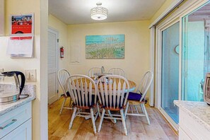 A dining area with a round table and chairs, a painting on the wall, and a view through a glass door. - Bayberry Woods townhouse with access to pool/tennis, fireplace & washer/dryer (Bethany Beach)