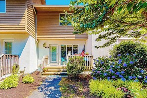 A two-story house with a front porch, a small garden with various plants, and a pathway leading to the entrance. - Bayberry Woods townhouse with access to pool/tennis, fireplace & washer/dryer (Bethany Beach)