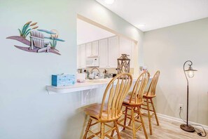 A dining area with wooden chairs, a white counter, and a kitchen in the background.