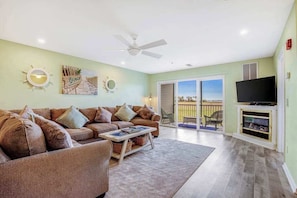 A living room with a sofa, coffee table, and a TV. There is a balcony with a view.