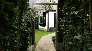 A pathway leading to a modern building with a glass entrance, surrounded by lush greenery. - Veluwse Oase | Sfeervol chalet op park de IJsvogel (Voorthuizen)