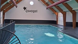 An indoor swimming pool with a high ceiling and wooden beams, a logo on the wall, and a staircase leading to the upper level. - Veluwse Oase | Sfeervol chalet op park de IJsvogel (Voorthuizen)