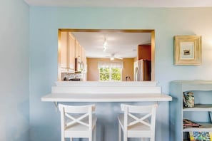 Una cocina con encimera blanca, dos sillas blancas y vista al comedor.