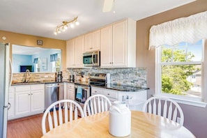 A modern kitchen with white cabinets, a microwave, and a dining area with a table and chairs.