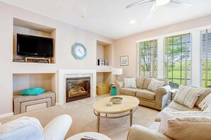 A living room with a fireplace, television, and large windows. - Bear Trap Dunes golf condo with indoor pool, 2 outdoor pools & beach shuttle (Ocean View)