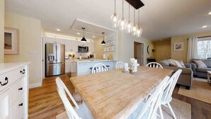 A modern kitchen with white cabinets, a wooden dining table, and hanging pendant lights. - Sea Colony ground floor condo, updated with fast WiFi, gas fireplace, & deck (Bethany Beach)
