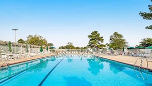 Ein Schwimmbecken mit Liegestühlen und Sonnenschirmen, umgeben von einem Zaun und Bäumen.