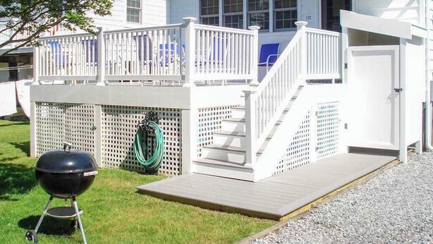 Een huis met een terras, een barbecue en een tuinslang.