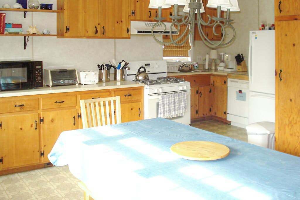 Una cocina con armarios de madera, microondas, estufa, lavamanos y una mesa con mantel.