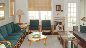 Een woonkamer met een groene bank, twee fauteuils, een salontafel, een boekenkast en een raam met een zonwering.