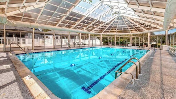 Ein Schwimmbad mit Glasdach, klarem Wasser und einer gefliesten Terrasse.