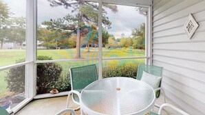 Eine überdachte Veranda mit Tisch und Stühlen, Blick auf einen Garten mit Bäumen und Rasen.