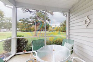 A covered porch with a table and chairs, a view of a yard with trees and a lawn.