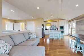 A spacious living room with a sofa, a kitchen area with bar stools, and a dining table. - Town of Fenwick island home on the water with dock & central A/C - dogs OK (Fenwick Island)