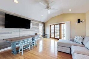 A spacious living area with a wooden dining table, benches, a sofa, a ceiling fan, and a large window. - Town of Fenwick island home on the water with dock & central A/C - dogs OK (Fenwick Island)