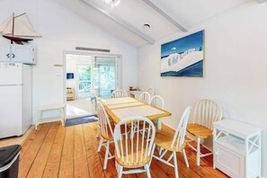 A dining area with a wooden table and white chairs, a white cabinet, and a painting on the wall.