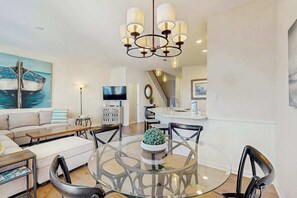 A modern living room with a round glass table, black chairs, a sofa, a TV, and a staircase leading to a kitchen. - Bear Trap Dunes home with washer/dryer, WiFi, pool, & sauna - near golf (Ocean View)