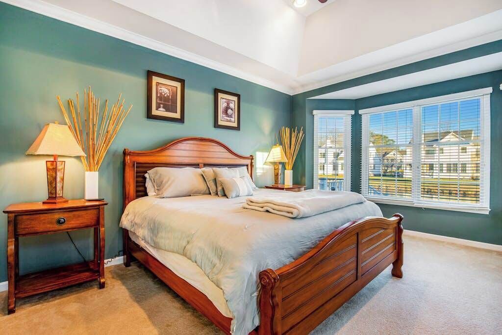 A bedroom with a wooden bed, two bedside tables, a window with blinds, and framed pictures on the wall.
