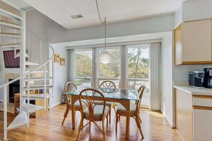 A modern kitchen with a glass dining table and chairs, a spiral staircase, and large windows. - Top-floor Sea Colony gem with AC & fast WiFi - walk to beach, pools & tennis (Bethany Beach)