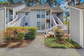 A two-story building with a central entrance, a covered porch, and a small garden area. - Top-floor Sea Colony gem with AC & fast WiFi - walk to beach, pools & tennis (Bethany Beach)