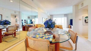 A modern living room with a glass dining table, wicker chairs, a sofa, and a TV. - Seaside Villas oceanfront townhome with 2 balconies, beach access & sunrise view (Fenwick Island)